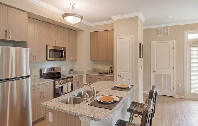 A kitchen with a refrigerator, microwave, oven, sink, and cabinets.