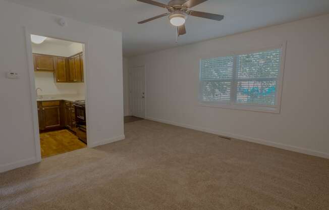 an empty living room with a ceiling fan and a kitchen