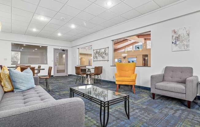 A living room with a grey couch, a yellow chair, a grey armchair, and a glass coffee table.