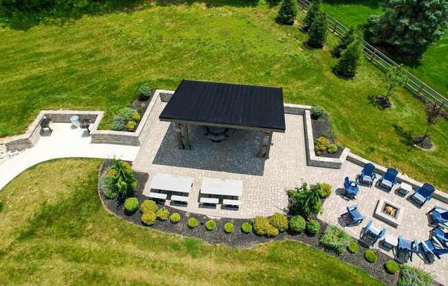A patio with a fire pit and chairs is surrounded by a grassy area.