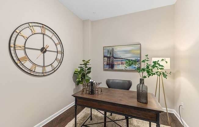 A large clock hangs on the wall above a table with a vase and a plant on it.