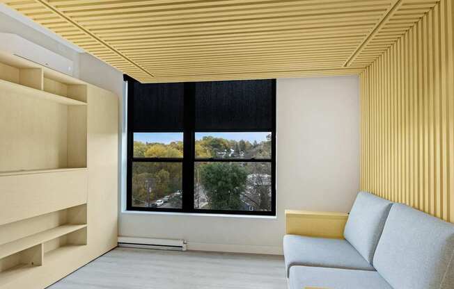 A modern living room with a yellow couch and a large window.