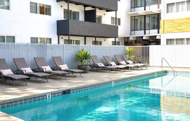 A pool with lounge chairs in front of a building.