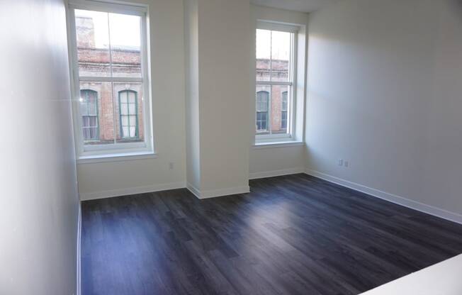 an empty living room with wood floors and two windows