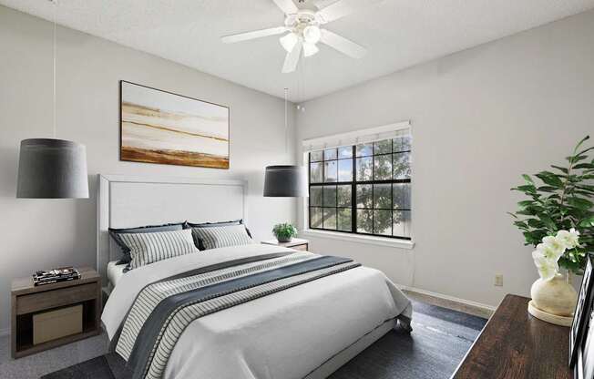 A carpeted bedroom in the B1 floorplan with a large bed, a ceiling fan, and a painting on the wall at Jefferson Creek Apartments in Irving, TX