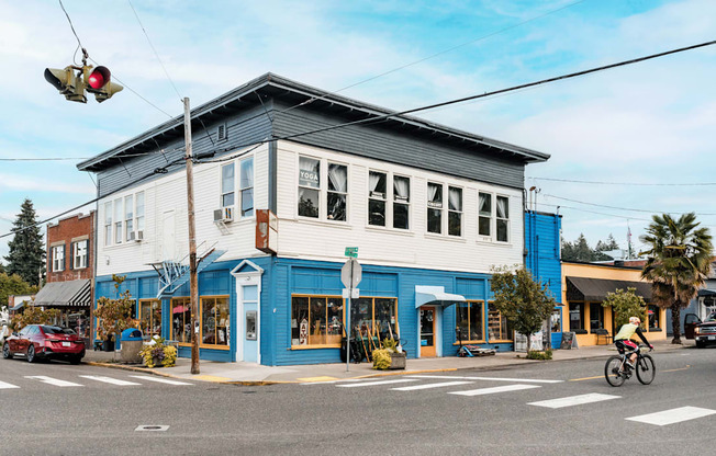 A cyclist is crossing the street in front of a blue building.