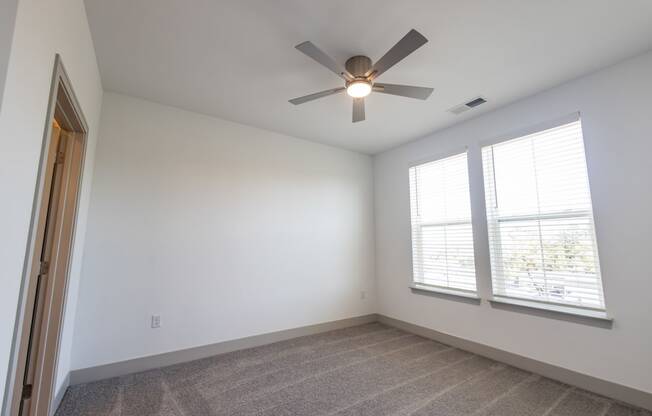 an empty room with a ceiling fan and two windows