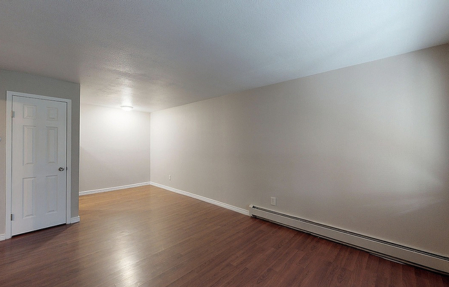 Bright, spacious living room with elegant hardwood floors and natural light from a large window, complemented by soft neutral walls.