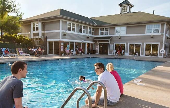 a group of people sitting at a pool with a building in the background