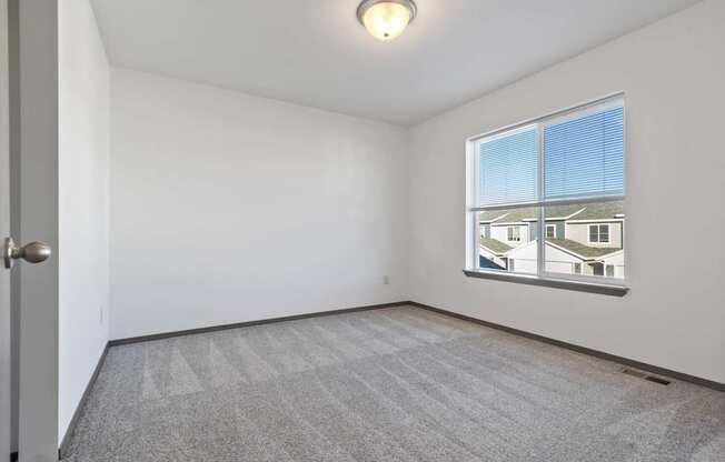 A room with a carpeted floor and a window showing a view of other buildings.