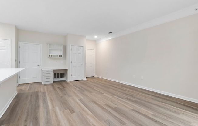 an empty living room and kitchen with white walls and wood flooring