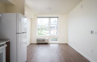 an empty living room with a refrigerator and a window