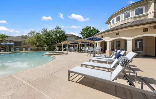 a pool and patio with chairs and umbrellas in front of a house