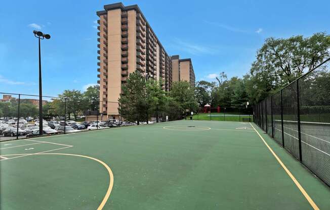 A basketball court is surrounded by a parking lot and apartment buildings.