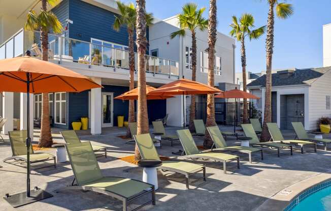 a group of lawn chairs and umbrellas near a pool and a house