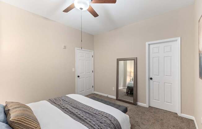A bedroom with a bed, a ceiling fan, and a mirror.