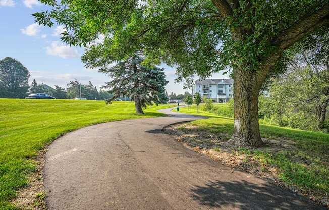 A tree-lined path in a park with a house in the background.