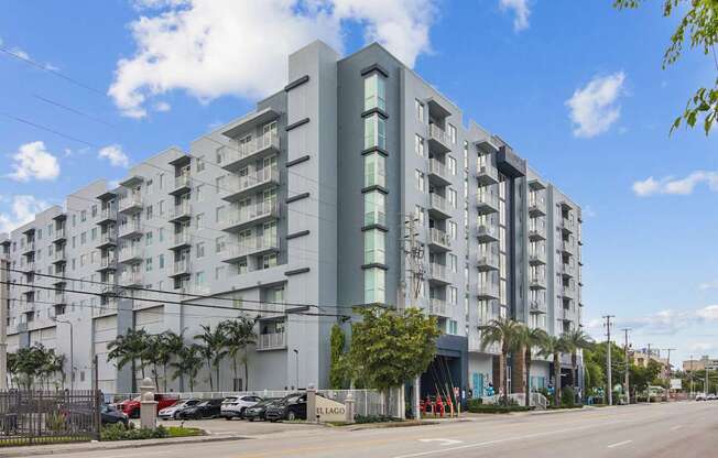 A modern apartment building with lush palm trees and a blue sky in the background at Blue Lagoon 7 Apartments in Miami, FL