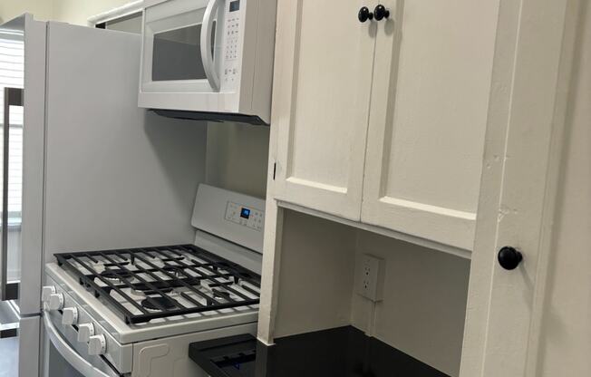 a small kitchen with white cabinets and a stove and microwave