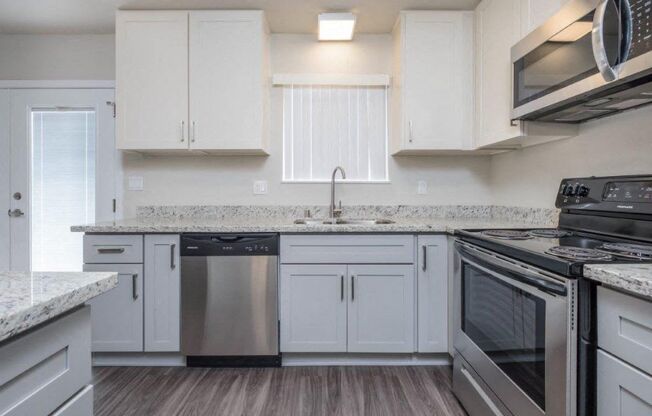 Closer look at kitchen with stone counters, white cabinets, stainless appliances, white cabinets, and window above sink