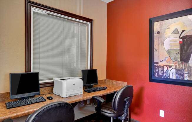 A desk with a computer monitor, keyboard, and printer in front of a window with blinds.
