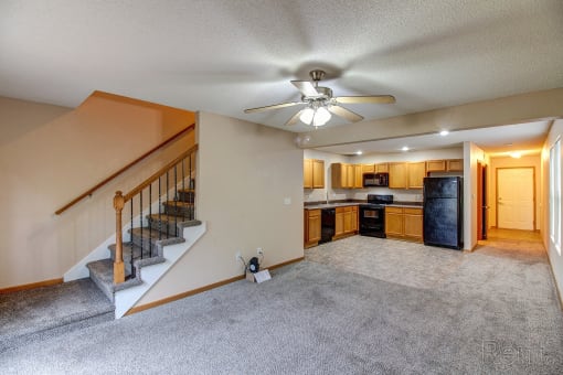 the living room and kitchen of a house with carpet and a ceiling fan