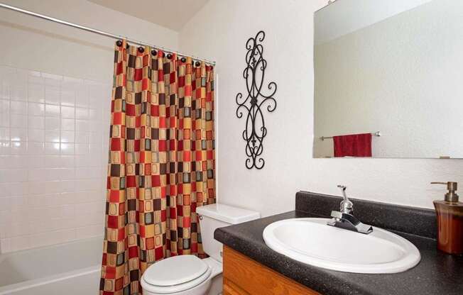 A bathroom with a white toilet, a black counter top, and a shower curtain with a pattern of squares and rectangles.