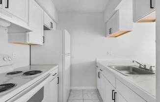 A white kitchen with a stove, sink, and cabinets.