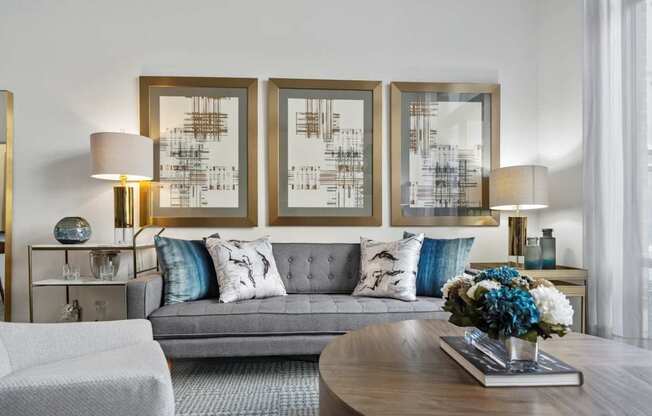 A modern living room with a grey sofa, a coffee table, and three framed artworks on the wall.