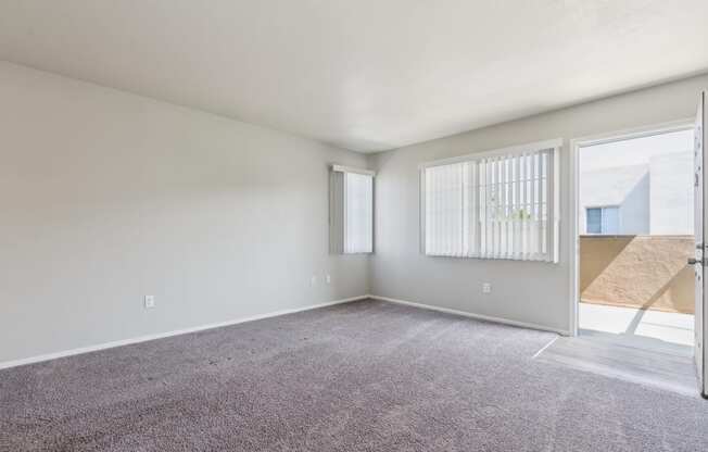 the living room of an apartment with carpet and a door to the patio