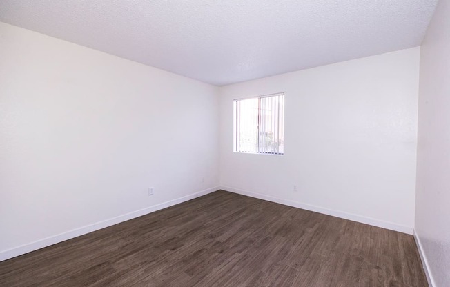 A room with wooden flooring and a window with blinds.