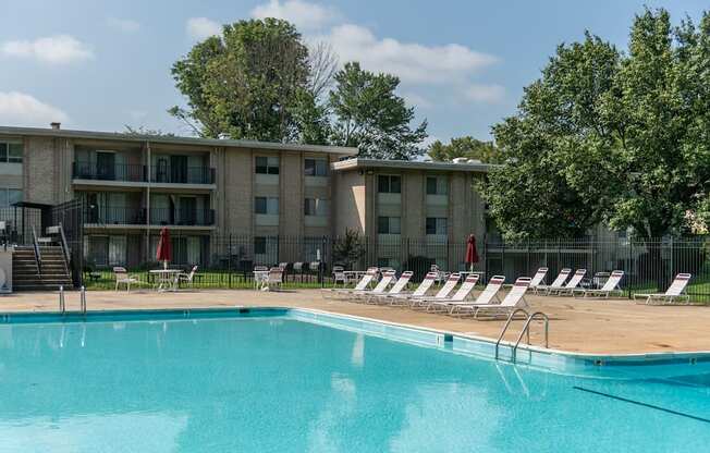 A swimming pool in front of a building with lounge chairs around it.