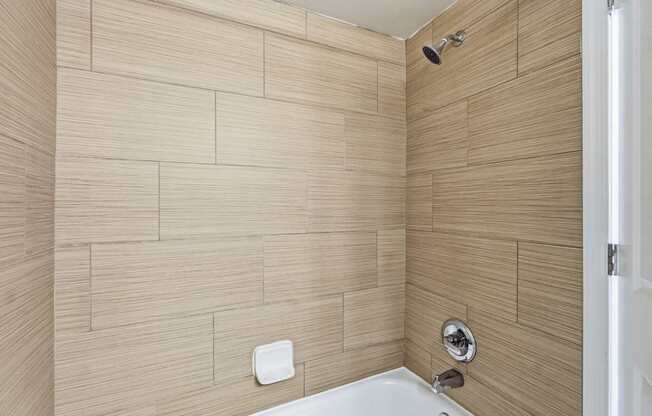 A white bathtub sits in a bathroom with tan tiled walls.