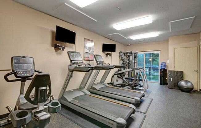 A modern fitness center here at Swan Creek with multiple treadmills, cardio machines, mounted TVs, and clean flooring, creating an energetic, convenient, and well-equipped workout space.