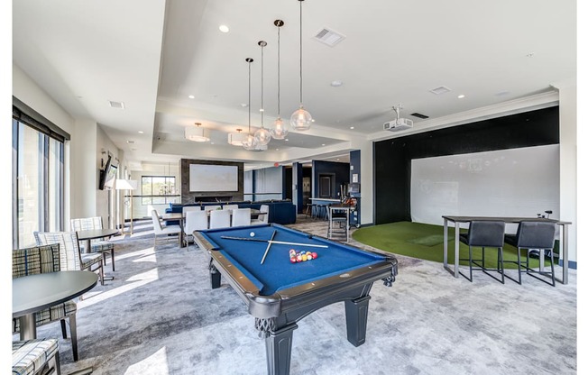 A pool table is in the middle of a room with a green rug and a dining table.