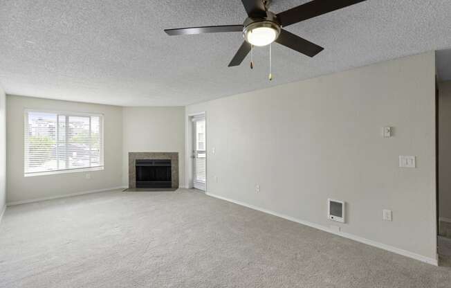 a living room with a fireplace, cozy carpeting, oversized windows, and a ceiling fan at Willows Court Apartment Homes, Seattle, WA