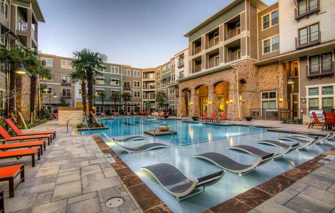 a swimming pool with chaise lounge chairs and palm trees in front of an apartment building