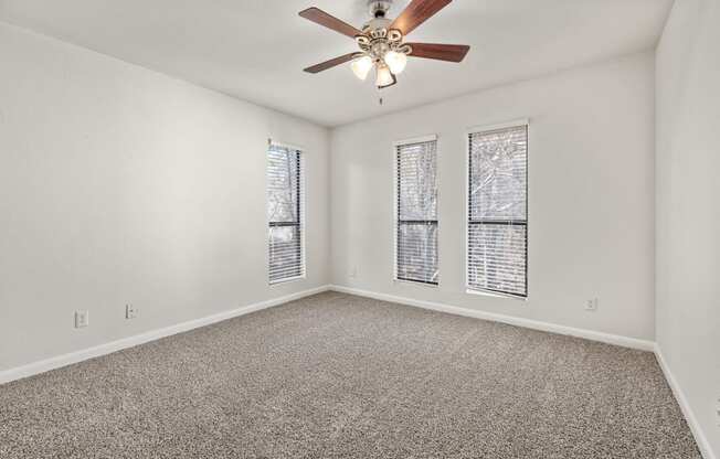 an empty living room with a ceiling fan and three windows