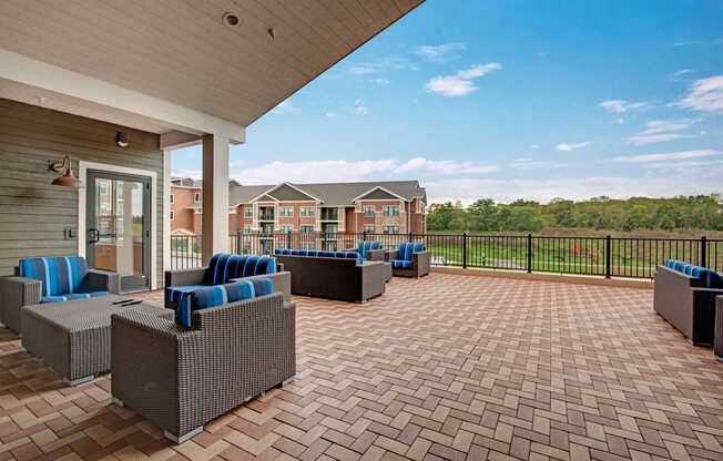 A spacious outdoor patio here at The Park featuring woven seating with blue striped cushions, wide open paver flooring, and scenic views, creating a bright, relaxing space for socializing and enjoying fresh air.