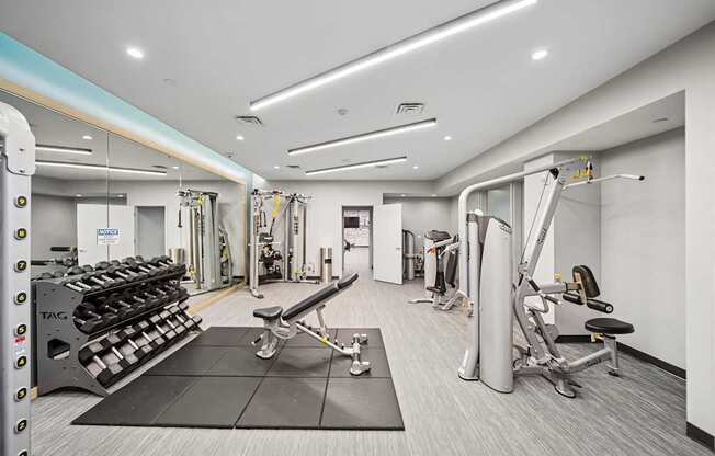 A gym with a variety of equipment including a squat rack, a bench, and a weight machine.