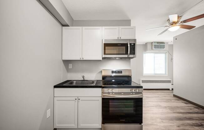 a kitchen with white cabinets and black appliances and a ceiling fan