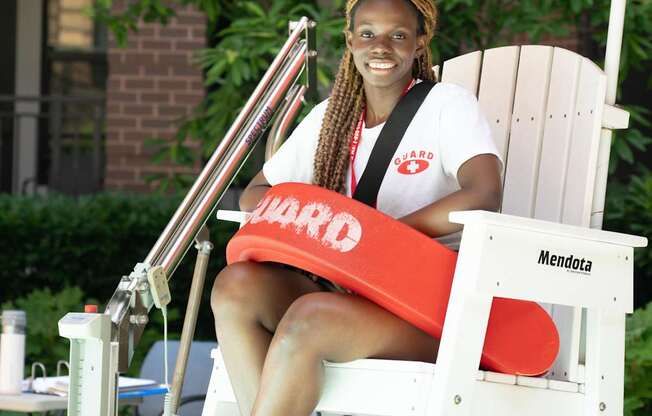A woman is sitting on a white chair with a red cushion and a red umbrella.
