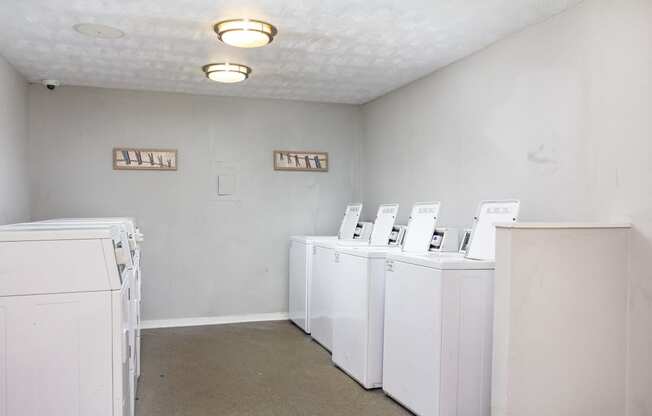 a row of white washers and dryers in an empty room