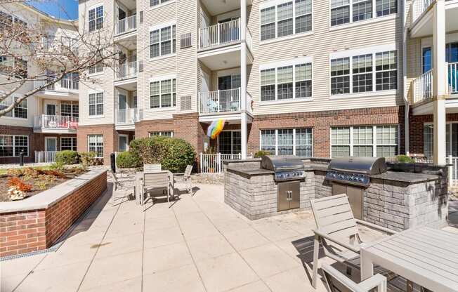 a patio with a grill and tables and chairs in front of an apartment building  at The Lena, Raritan, 08869