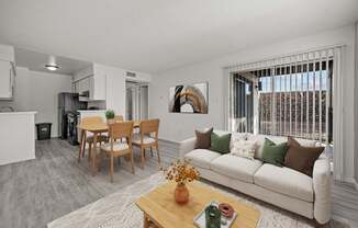 A living room with a white couch, a wooden coffee table, and a dining table with chairs.