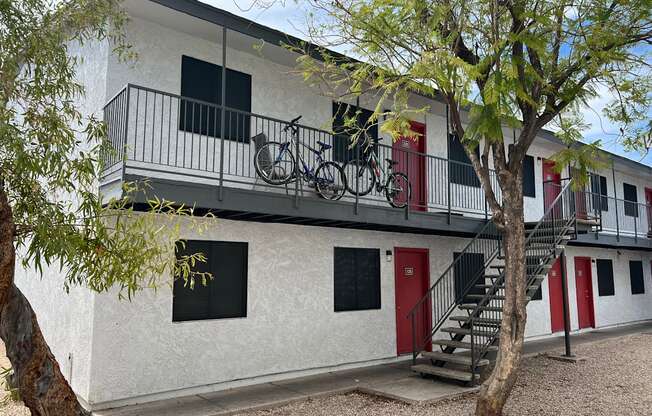 A white building with a red door and a bicycle hanging on the balcony.