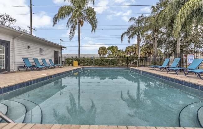 a pool with blue chairs and palm trees next to a house