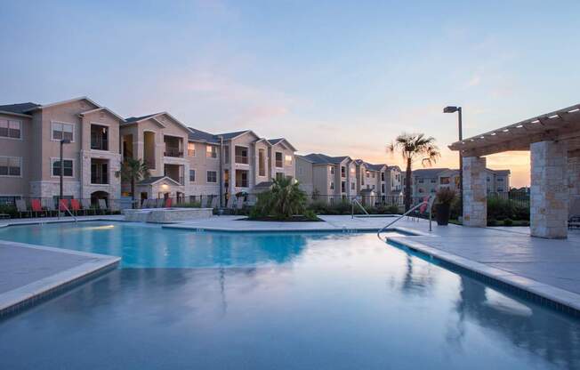 A swimming pool in front of apartment buildings at dusk.