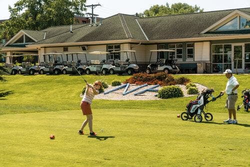 Two golfers enjoying the lush golf course in the sun with a building in the background.