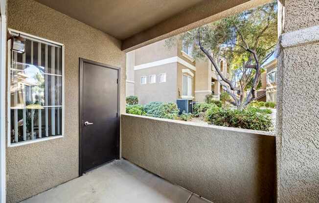 A balcony with a door and a window overlooking a building and trees.